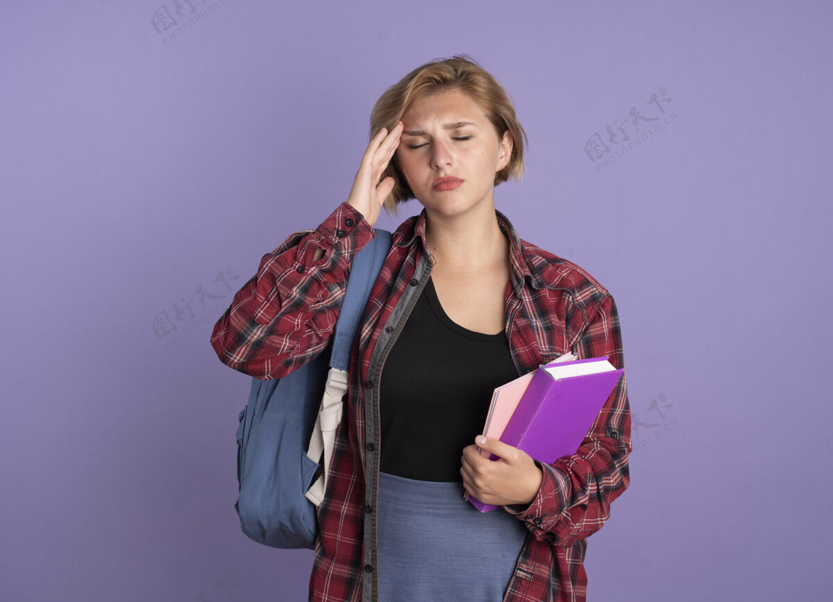 疼疼痛的年轻斯拉夫学生女孩背着背包 手放在额头上 手里拿着书和笔记本学生紫色拿着