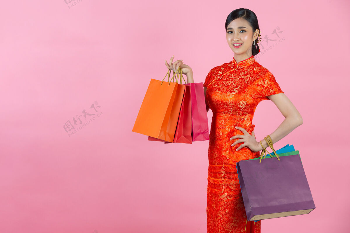 东方美丽的亚洲女人快乐的微笑和购物在中国新年的粉红色背景展示年空白