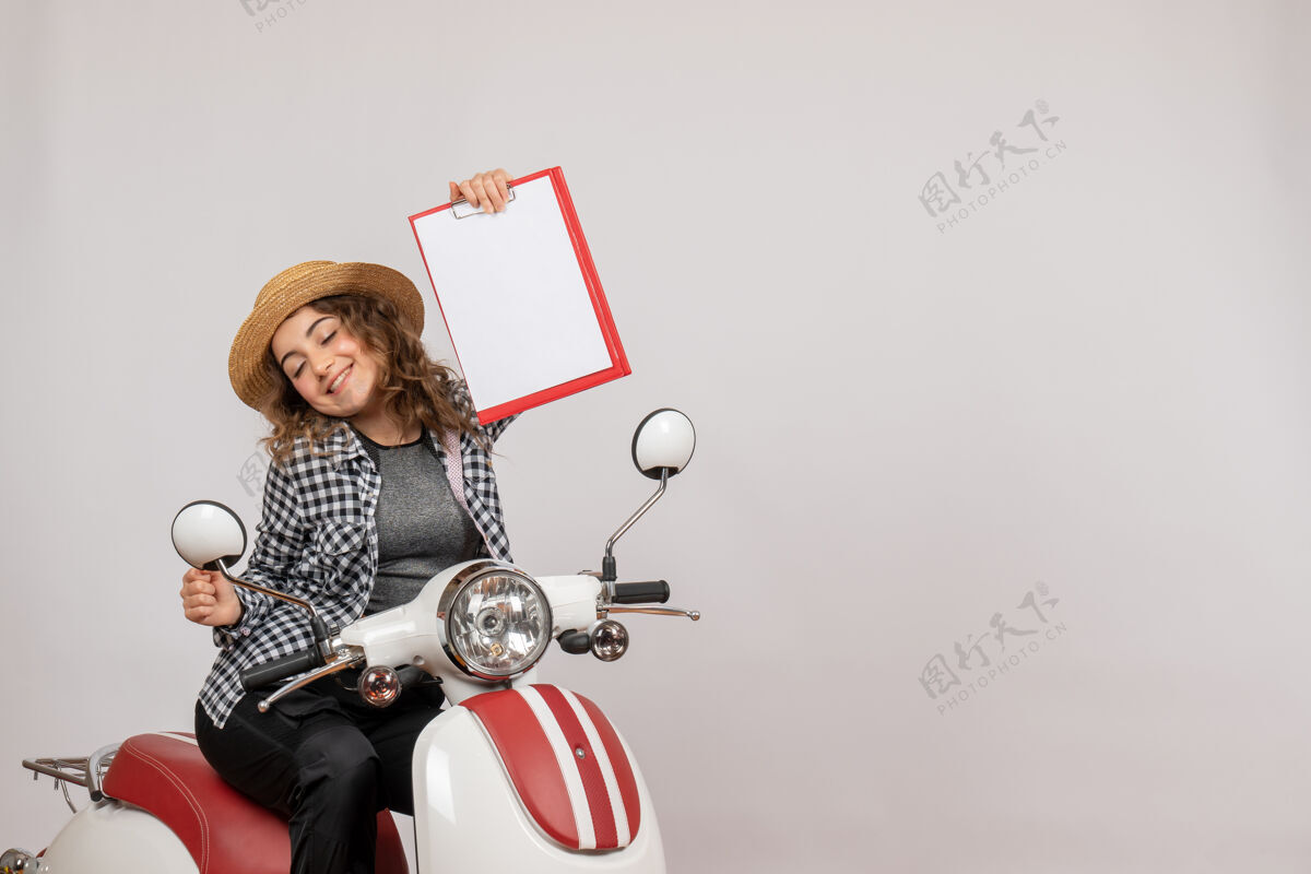 人坐在轻便摩托车上微笑的旅行女孩举着红色的剪贴板红色肖像剪贴板