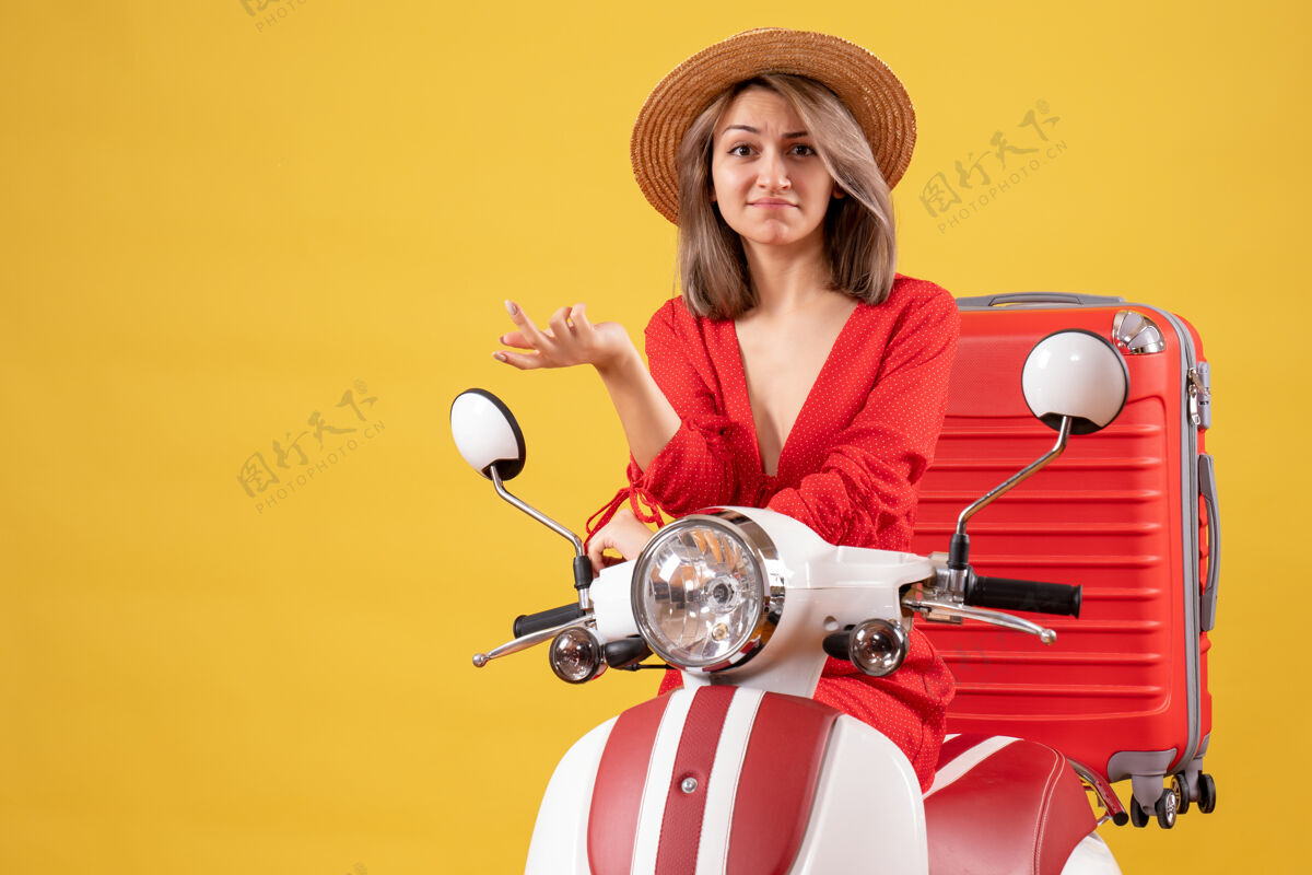 婴儿带着手提箱坐在轻便摩托车上迷惑不解的漂亮女孩成人人模特