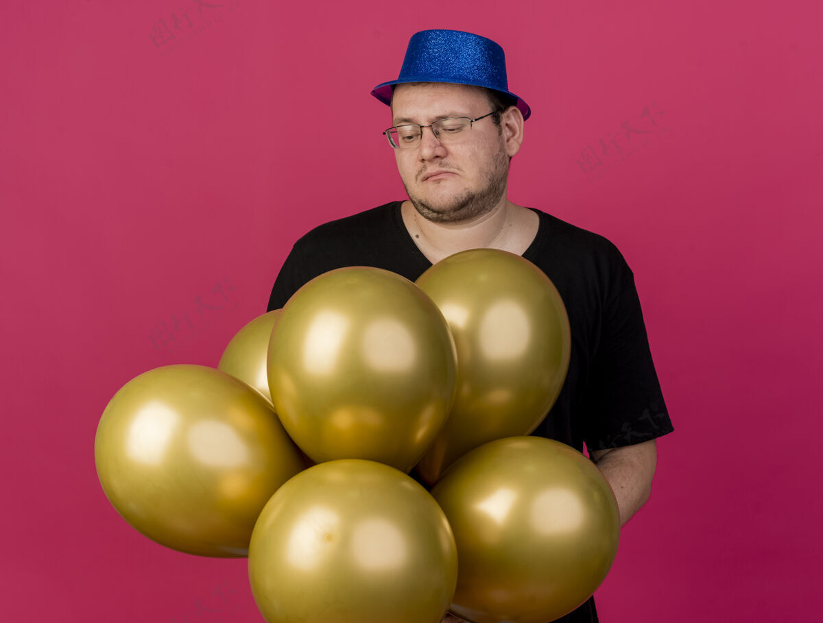男人失望的成年斯拉夫人戴着眼镜 戴着蓝色派对帽 手里拿着氦气球粉色失望气球