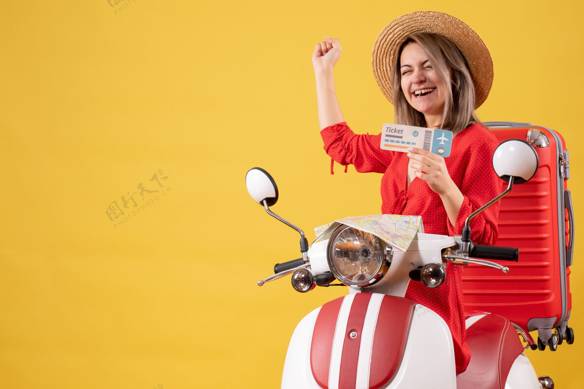 成人一位穿着红裙子的年轻女士 骑着轻便摩托车 手里拿着车票 高兴极了衣服时尚肖像