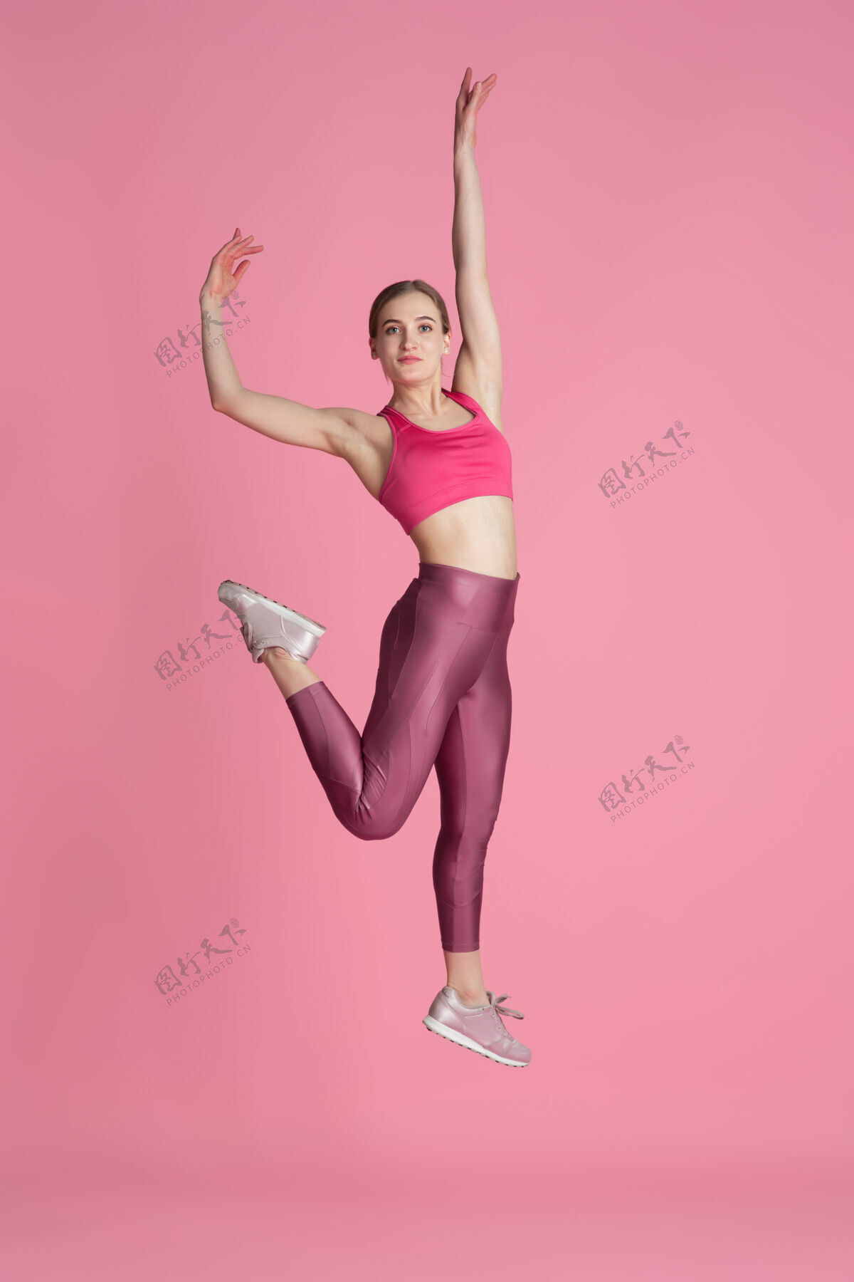 健康在跳跃美丽的年轻女运动员在工作室练习 单色粉红色肖像练习舞蹈人