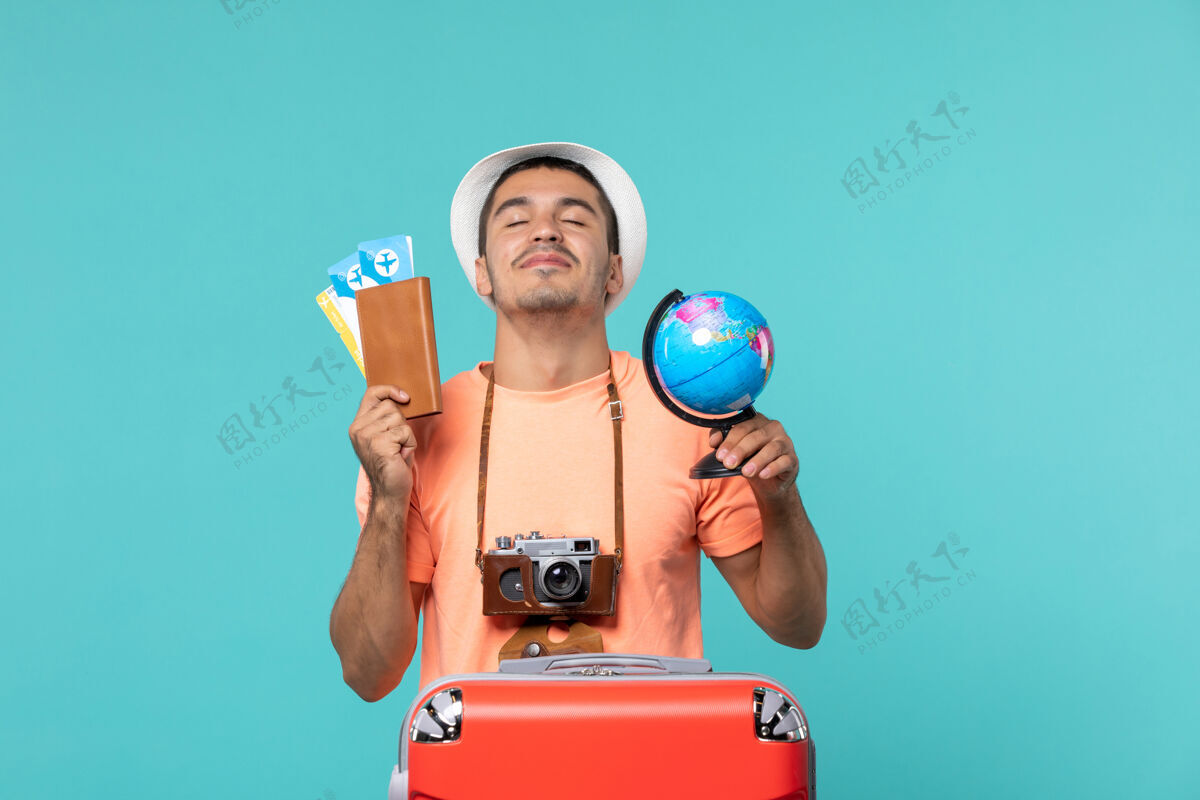 小正面图男性在度假时拿着小地球仪和蓝色的门票蓝色旅行男人