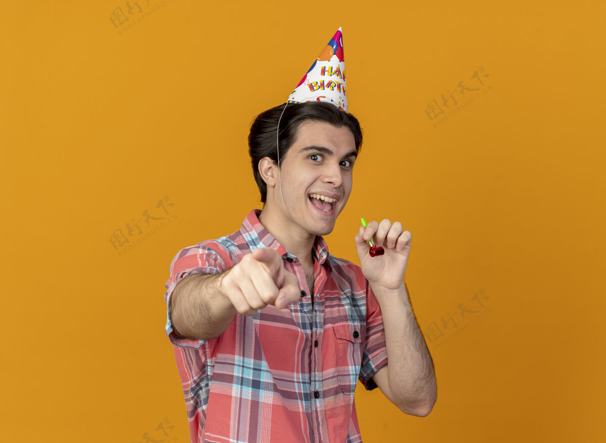 复制快乐英俊的白种人戴着生日帽手持派对哨子指着镜头男人橙色举行