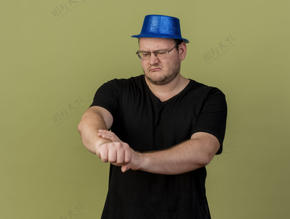 蓝色一个戴着眼镜 戴着蓝色派对帽的未获释的成年斯拉夫男子握着并看着自己的手臂橄榄色斯拉夫光学