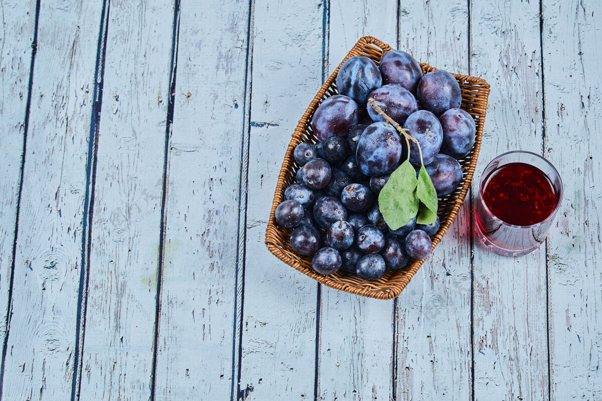 有机用一杯果汁把李子放在蓝色的篮子里花园健康紫色