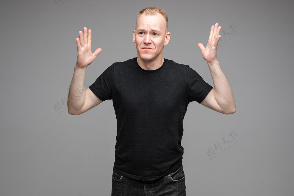手势困惑和悲伤的男子在黑色衬衫举起手在空中 而在灰色的背景摆姿势黑色衬衫男性成人