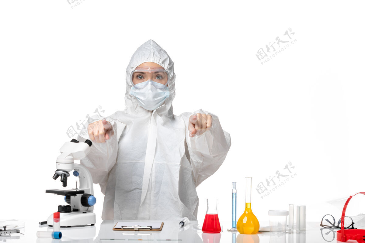 专业正面图年轻女医生穿着白色防护服 戴着口罩 由于柯维德指向白色背景病毒大流行飞溅柯维德-医学大流行病毒