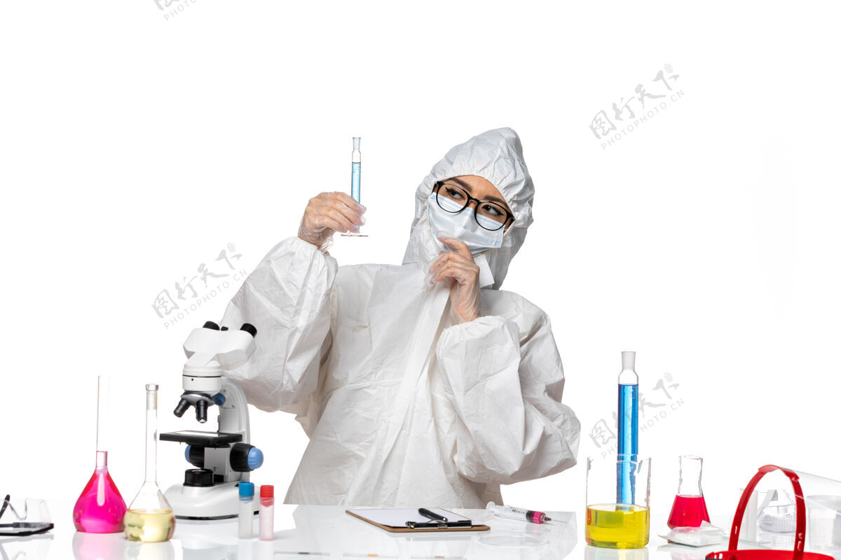 化学正面图身穿特殊防护服的年轻女化学家拿着浅白色背景上蓝色溶液的烧瓶实验室冠状病毒化学病毒防护容器实验室外套
