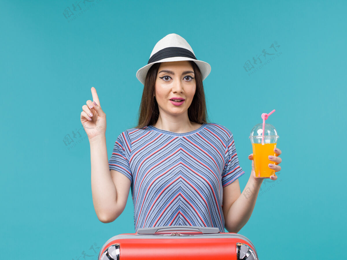 举行前视图：度假中的女人拿着她的红包 拿着她的果汁在蓝色的书桌上旅行旅行度假女性旅行肖像果汁旅行