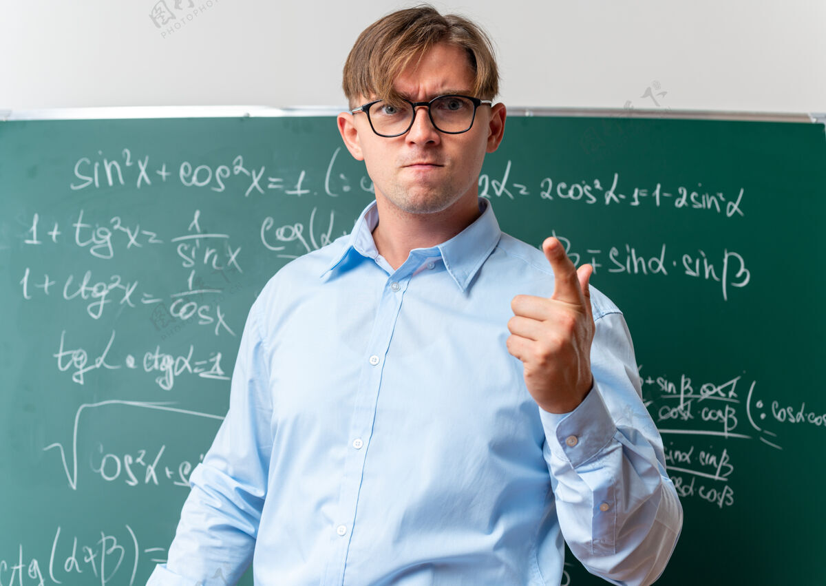 数学戴着眼镜的年轻男老师站在教室里的数学公式黑板旁 神情不快 怒气冲冲靠近老师男