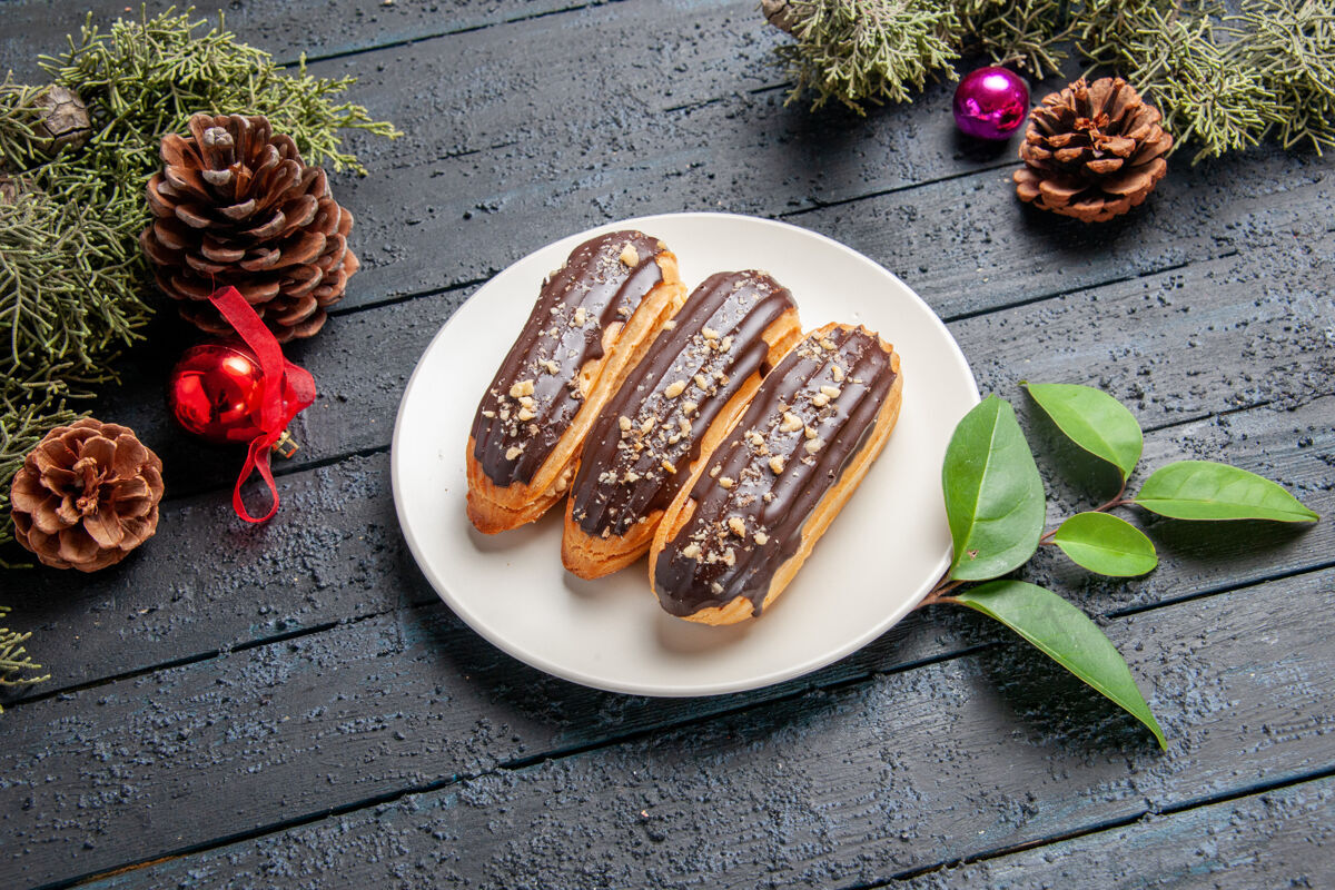 叶子底视图巧克力eclairs在椭圆形板松果圣诞玩具冷杉树叶在黑暗的木制地面午餐黑烧烤