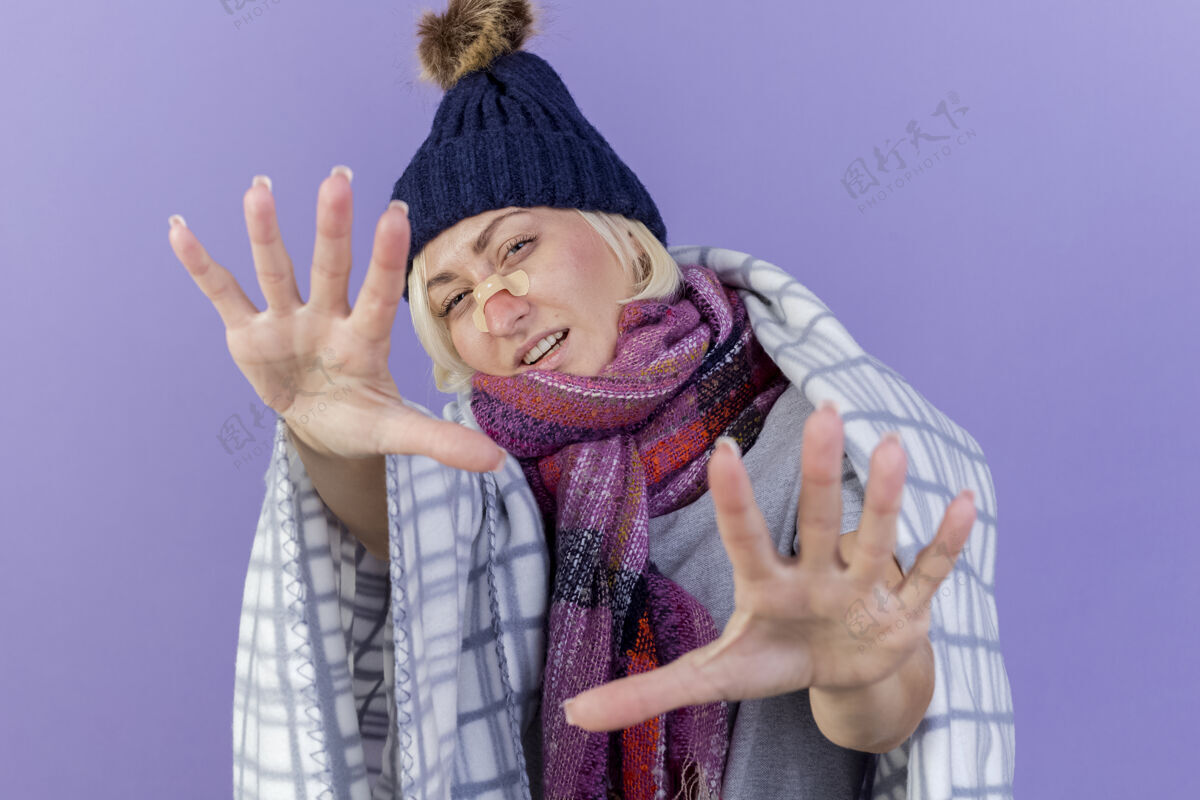 年轻自信的年轻金发病斯拉夫女人鼻子上贴着医用膏药戴着冬天的帽子和围巾医学手拉伸