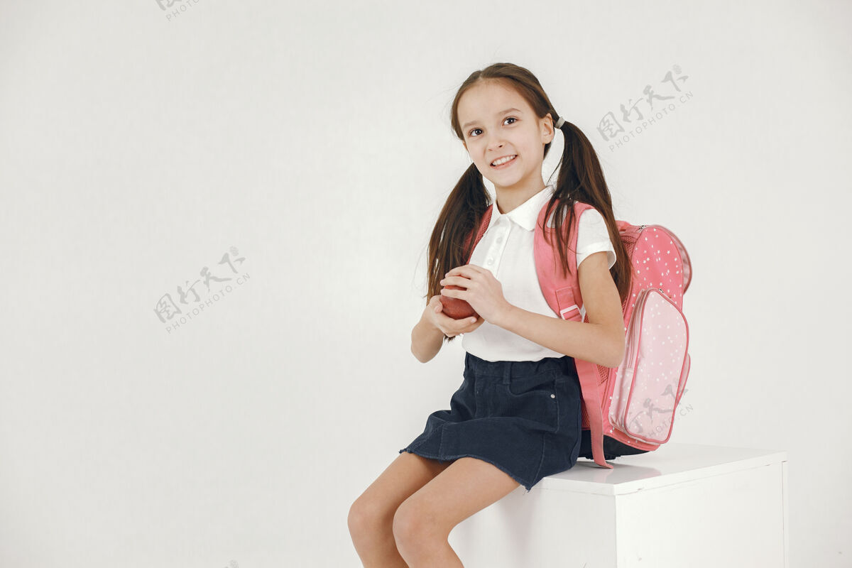 漂亮女学生坐在白色的立方体上背着书包的女孩拿着苹果坐在白色的立方体上女性文学快乐