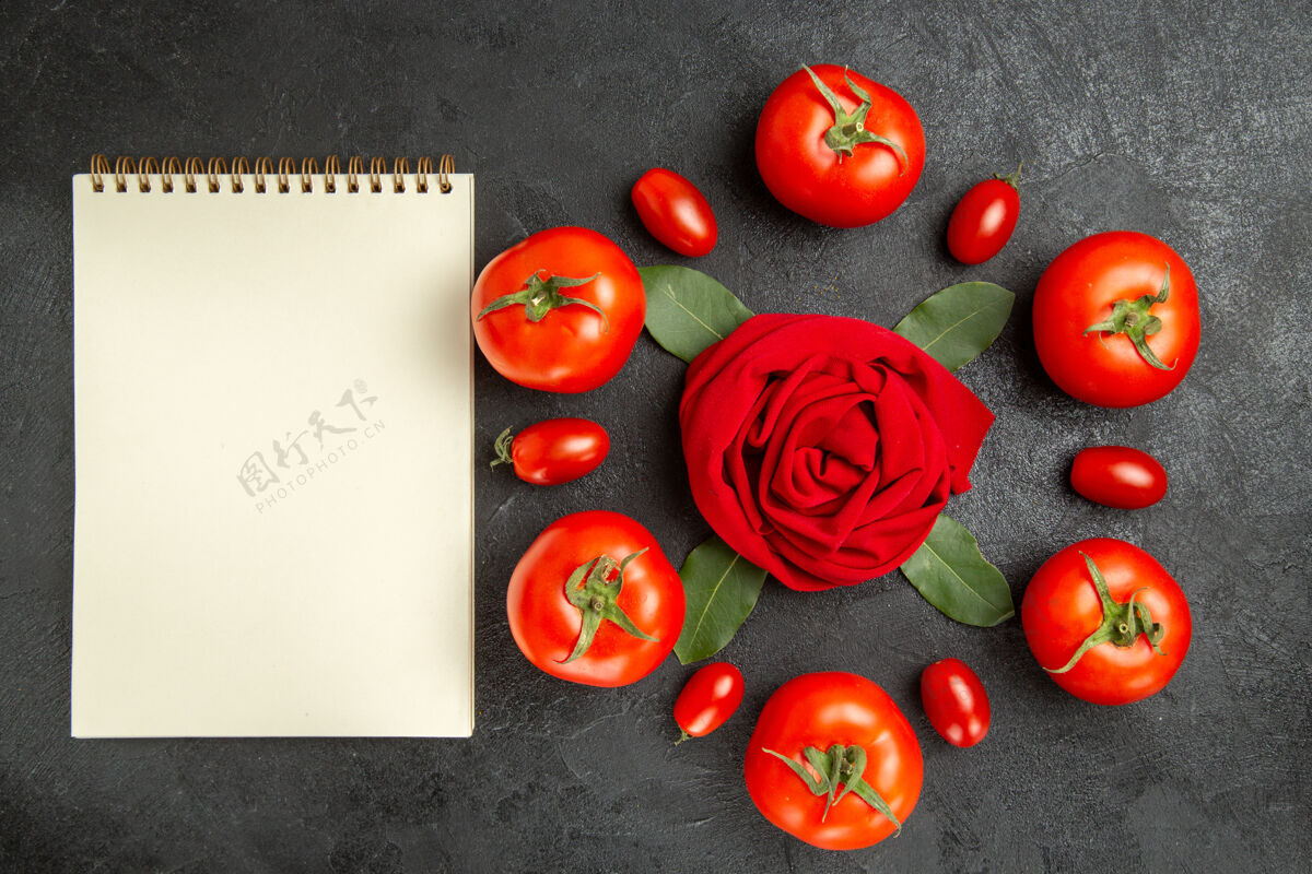 成熟的俯视图红色和樱桃西红柿围着玫瑰形的毛巾和月桂叶 在黑暗的地面上放着一本笔记本毛巾蔬菜生的