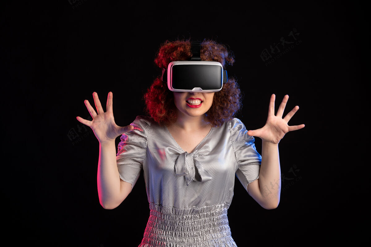 姿势年轻女性戴着虚拟现实耳机在黑暗的表面现实肖像年轻女性