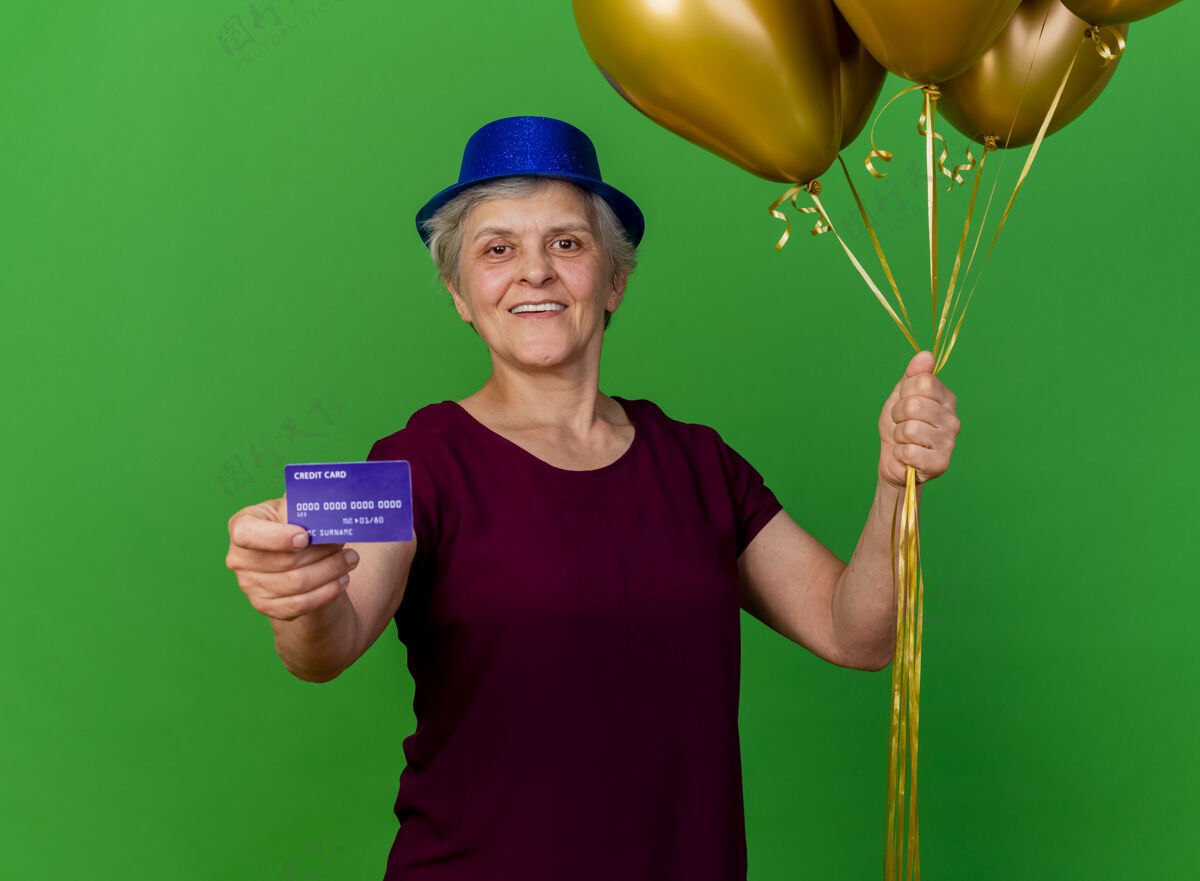 帽子微笑的老妇人戴着聚会的帽子 手里拿着信用卡和氦气球女人氦气球