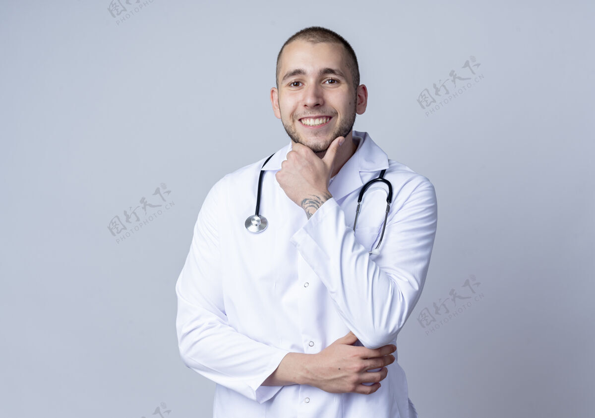 穿着微笑着的年轻男医生 穿着医用长袍 脖子上戴着听诊器 触摸着隔离在白墙上的下巴脸男性脖子