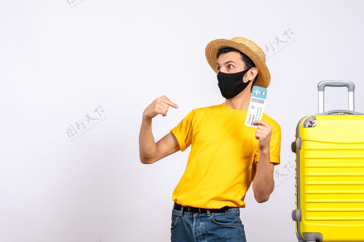 站着正面图：穿着黄色t恤的年轻人站在黄色手提箱旁 拿着旅行票指着自己男人T恤抱着