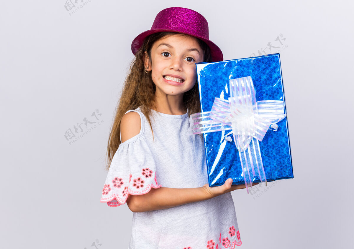 女孩微笑的白人小女孩 戴着紫色派对帽 拿着礼品盒 隔离在白色墙壁上 留着复制空间帽子小微笑