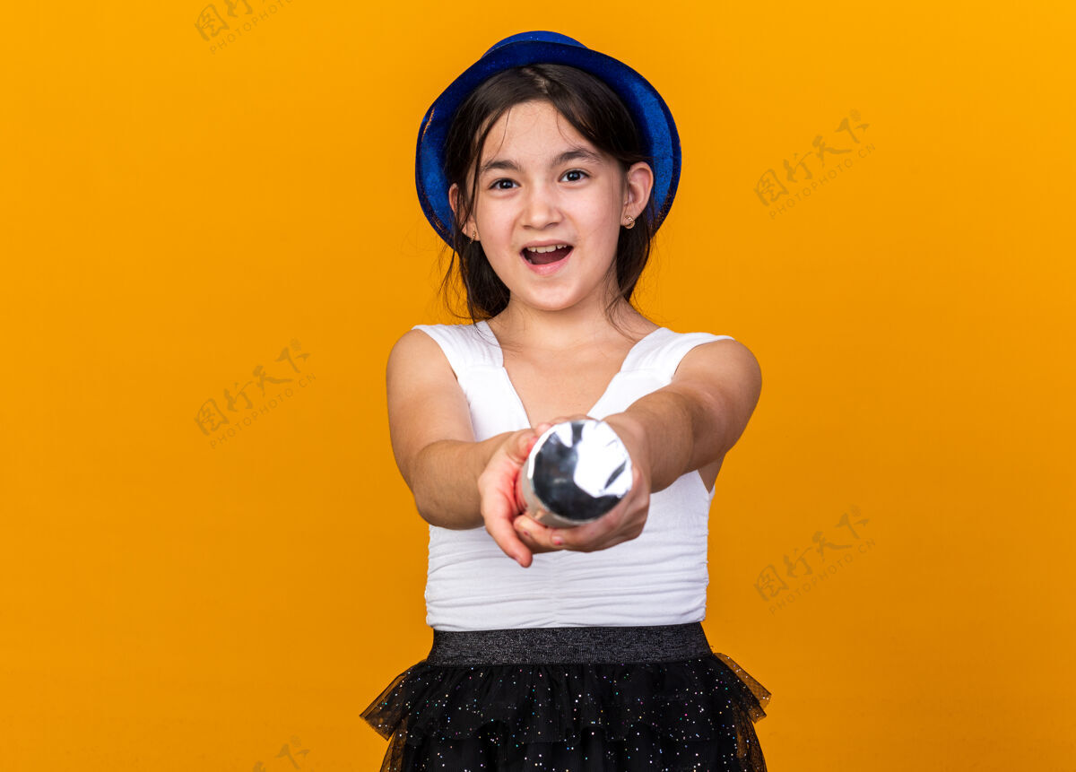 五彩纸屑快乐的年轻白人女孩 戴着蓝色派对帽 手持五彩纸屑大炮 被隔离在橙色的墙上 还有复制空间大炮喜悦持有