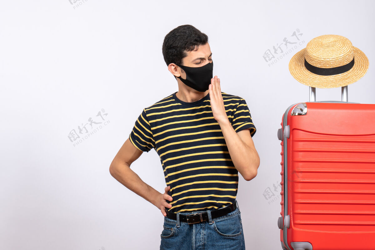 前面正面图：站在红色手提箱旁打着哈欠 戴着黑色面具的年轻游客男红成人