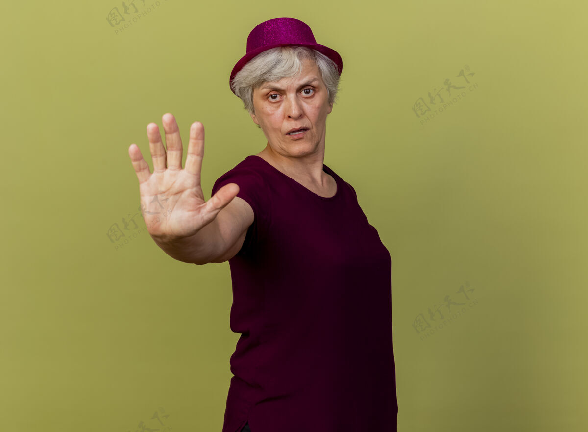手自信的老妇人戴着聚会帽 手势停止手势孤立在橄榄绿的墙上姿势表情女人