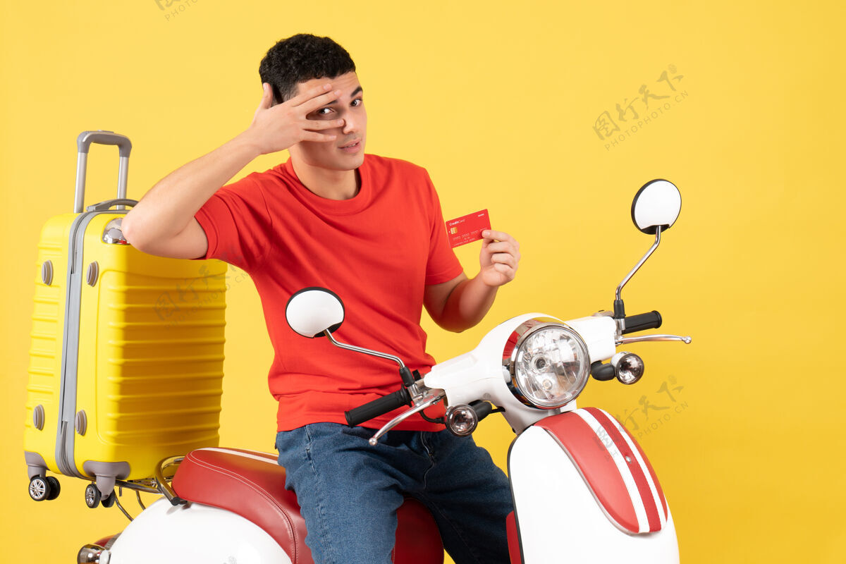男人前视图骑着轻便摩托车的年轻人拿着黄色背景的信用卡男性人信用卡