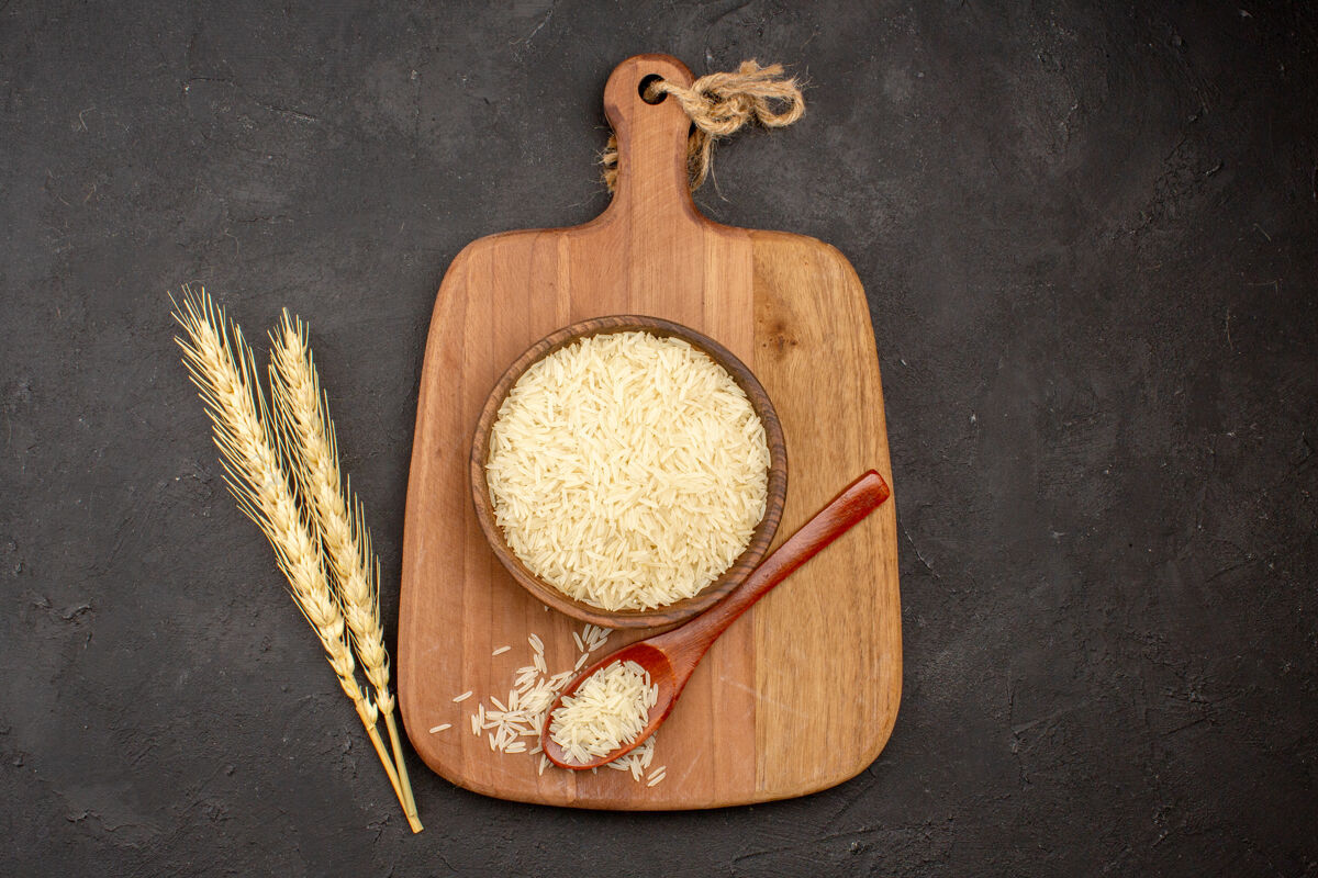 烹饪深灰色表面上棕色木板内生米的俯视图新鲜美味晚餐