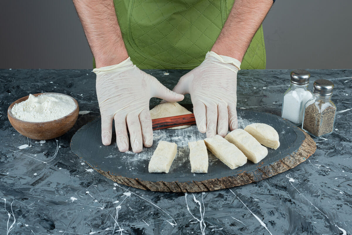 烘焙男人戴着手套在大理石桌上做面团制作生的面包