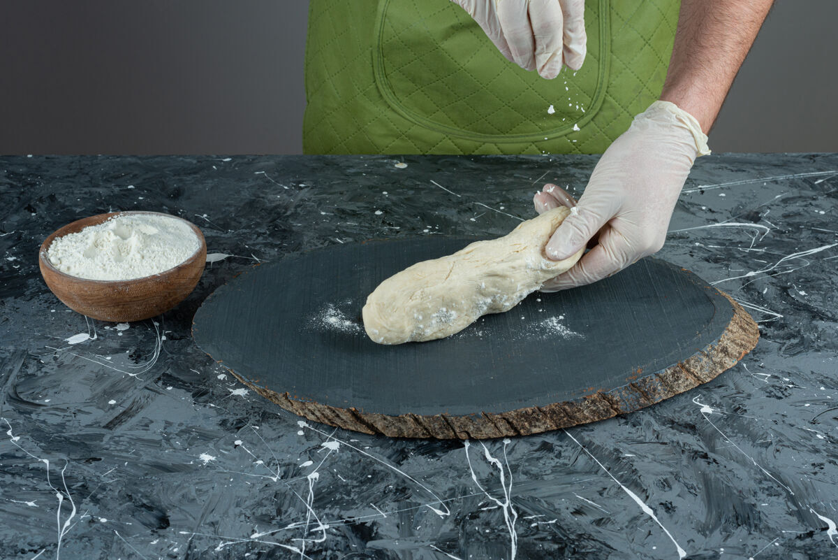 生的男人戴着手套在大理石桌上做面团制作烹饪手