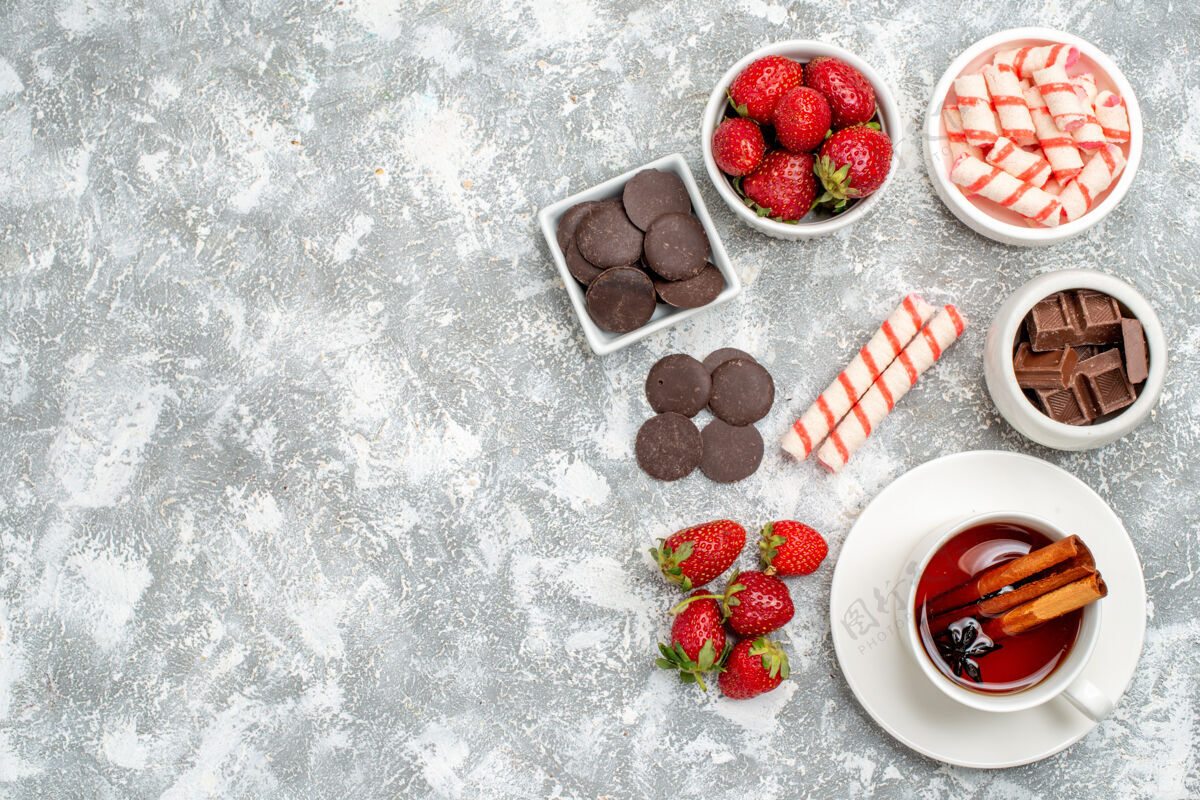 茶顶视图碗草莓巧克力糖果和肉桂茴香种子茶在灰白色的地面右侧水果肉桂新鲜