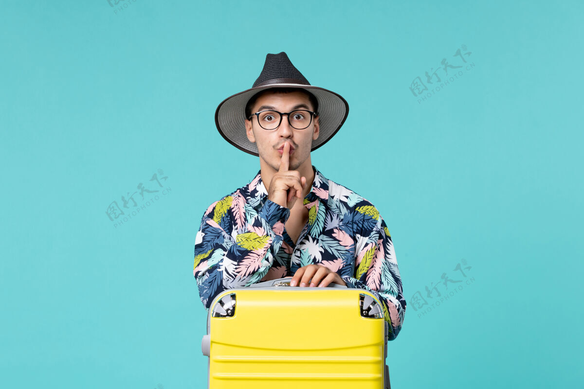 快乐年轻男子正拿着他的黄色袋子准备在蓝色的墙上旅行旅行旅行帽子