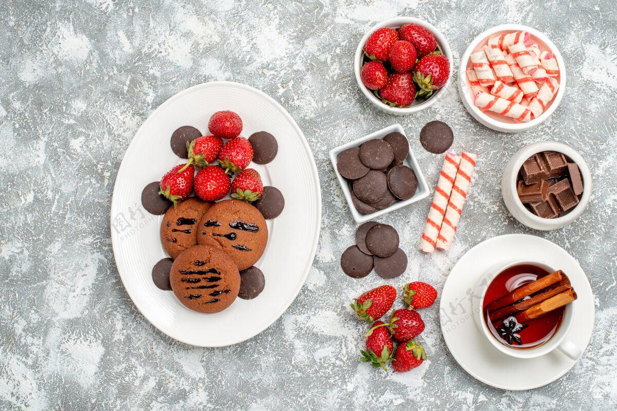食物在灰白色的地面上 可以俯瞰带有糖果草莓巧克力糖果和一些草莓糖果巧克力以及一杯茶的碗新鲜的草莓磨碎的