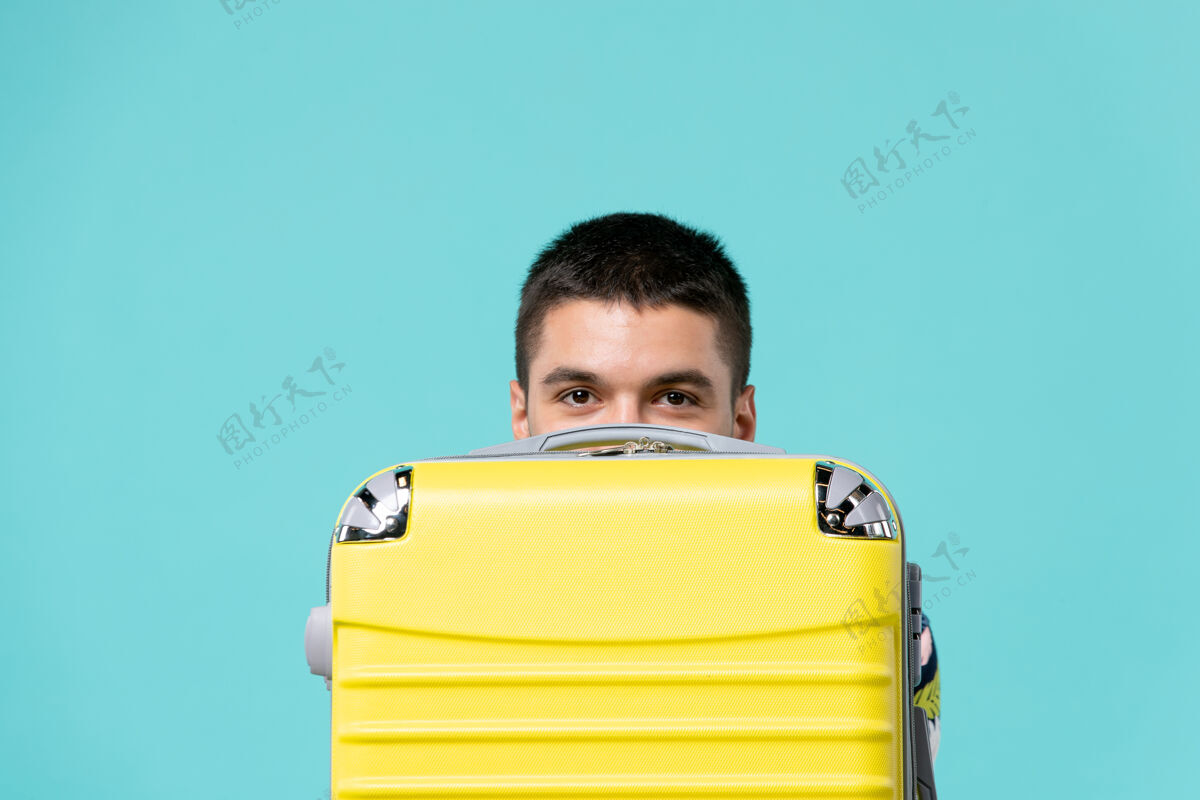 前面年轻的男性正准备度假 黄色的袋子藏在蓝色的墙上旅行假期旅行