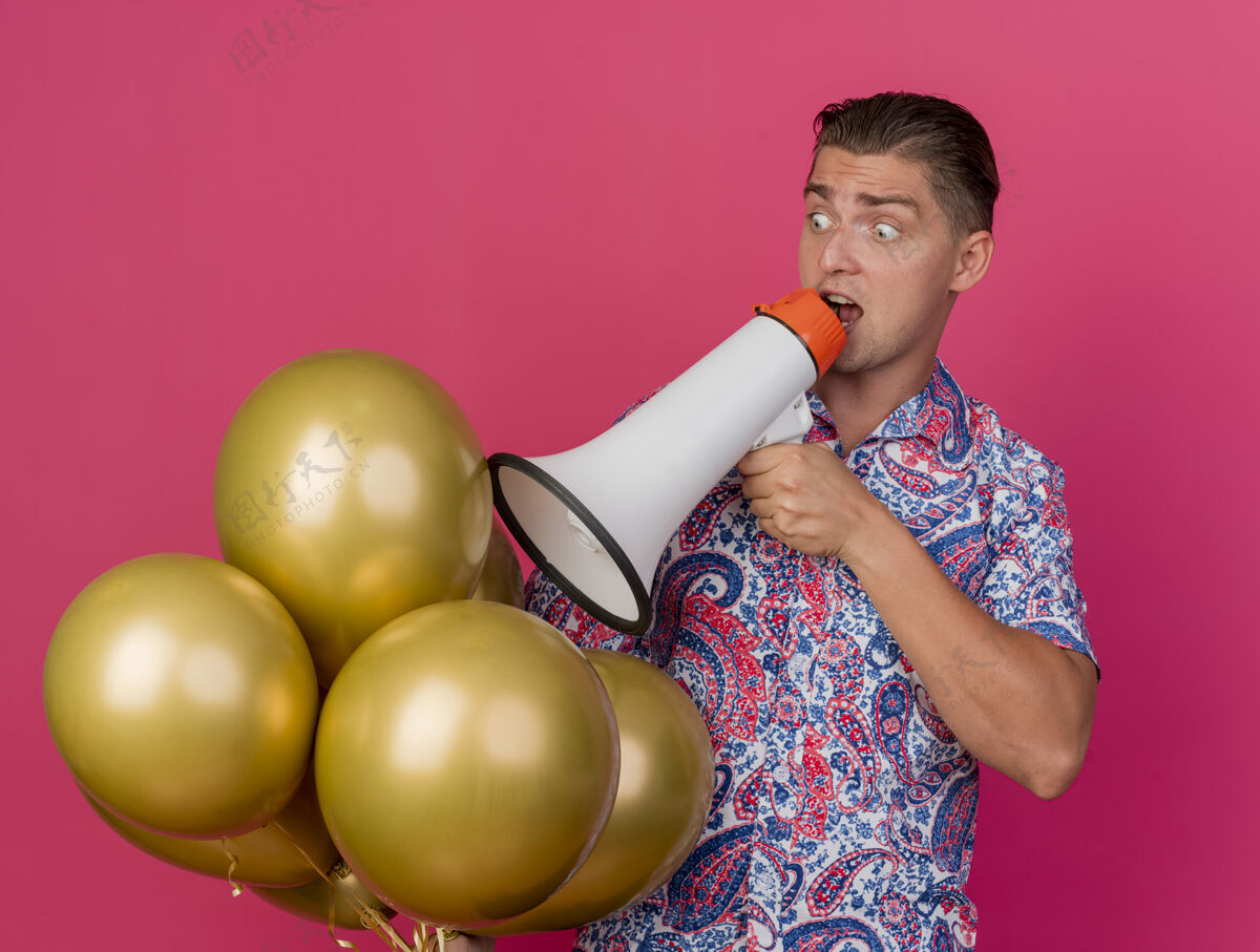 气球吓坏了的年轻人一边看一边穿着五颜六色的衬衫拿着气球 一边用扬声器说话 粉红色的脸上孤立着派对扩音器穿