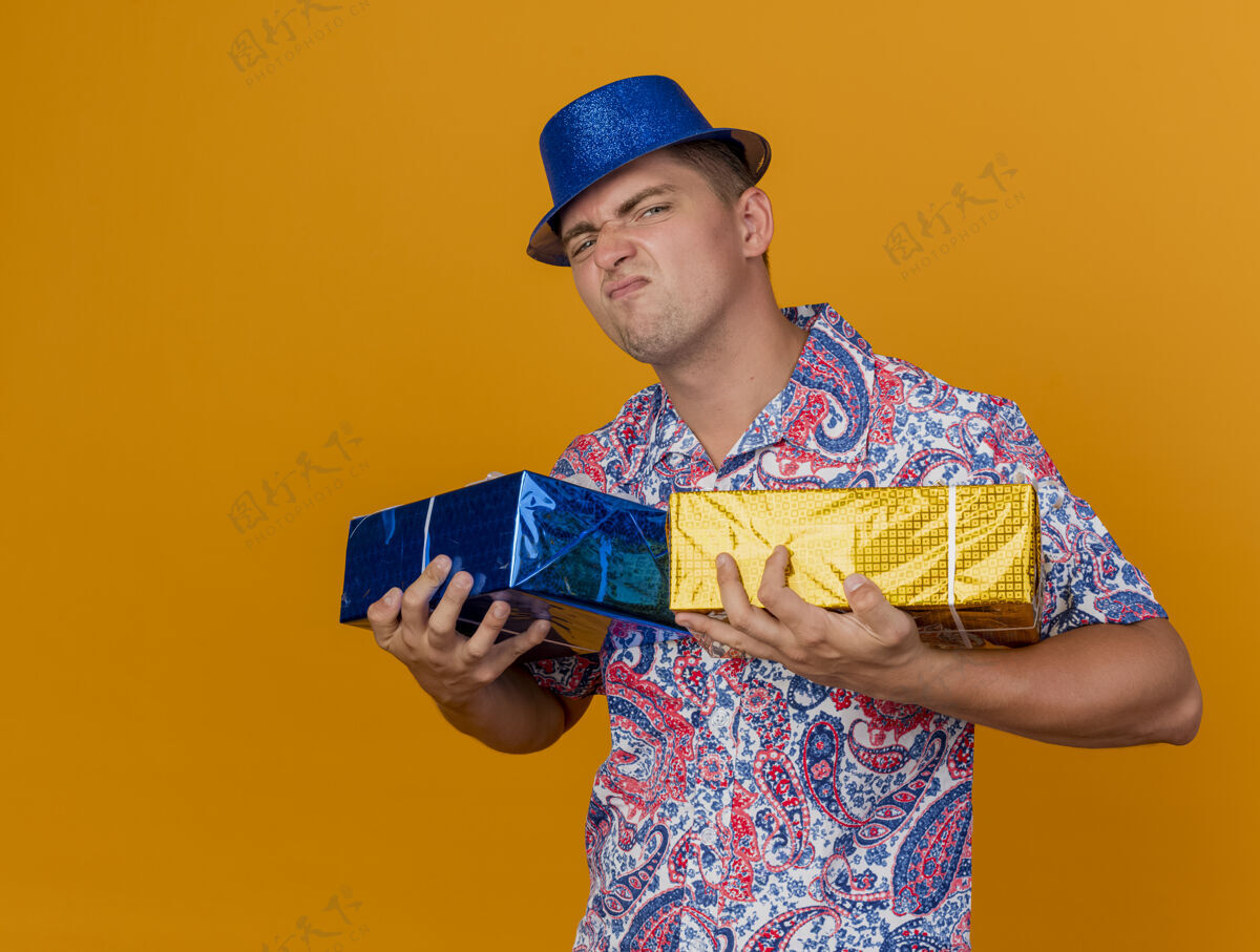 抱着贪婪的年轻人戴着蓝帽子拿着礼品盒孤立在橙色礼物帽子橙色