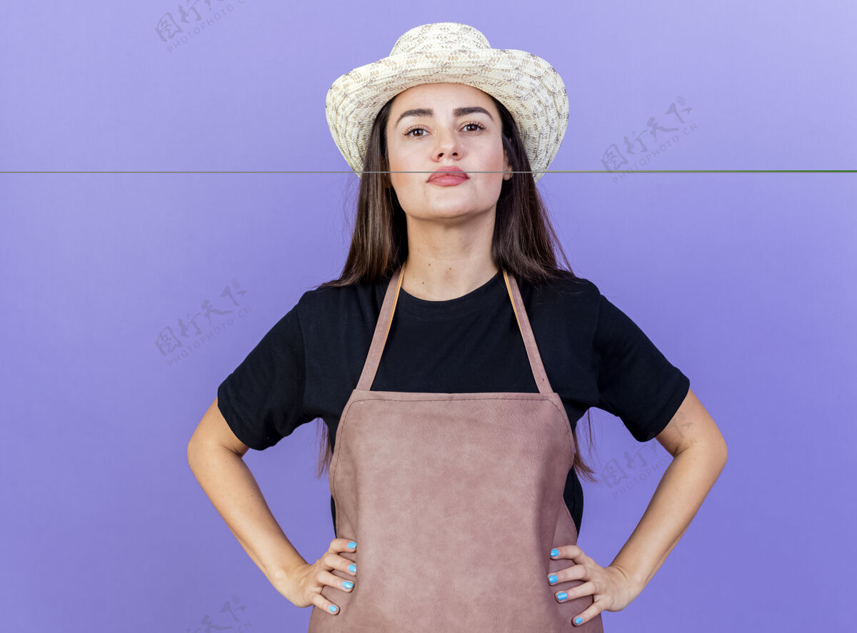 穿着自信美丽的园丁女孩穿着制服戴着园艺帽把双手放在臀部隔离在蓝色臀部帽子制服