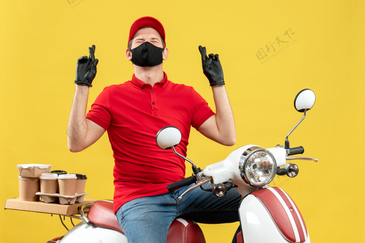 手套顶视图充满希望的梦想年轻人穿着红色上衣 戴着帽子手套 戴着医用面罩 坐在黄色背景的踏板车上传递命令男性摩托车帽子