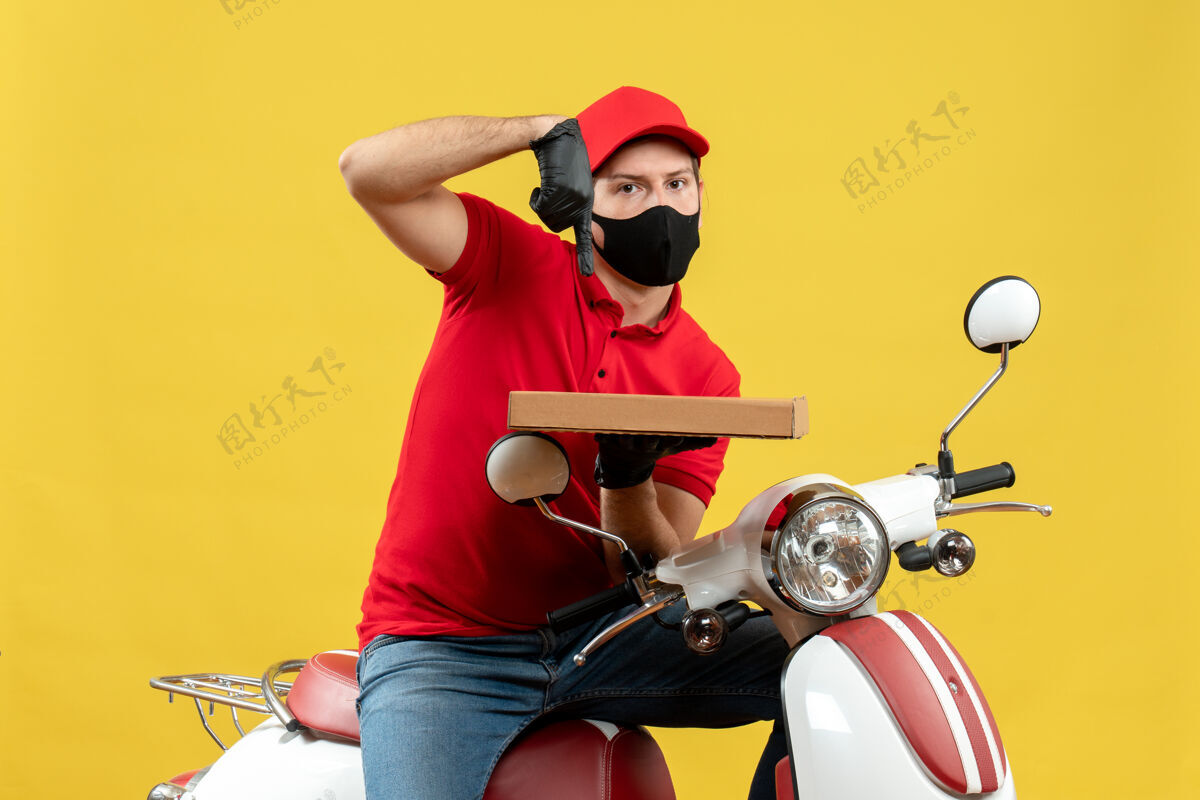 人俯视图：忙碌的快递员身穿红色上衣 戴着帽子手套 戴着医用面罩 坐在滑板车上指点秩序手套头盔坐着