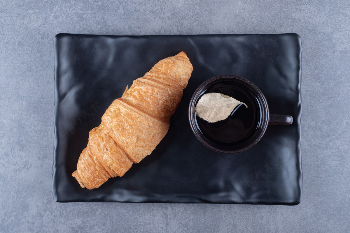 新鲜咖啡和羊角面包在黑色盘子上的俯视图面包卷面包营养