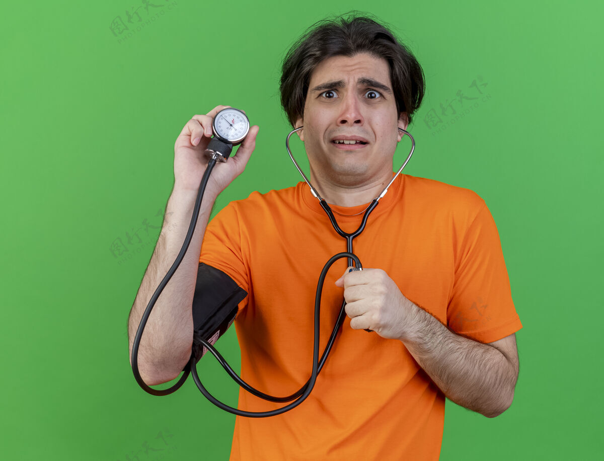 男人年轻人戴着听诊器拿着血压计隔离在绿色血压计关心抱着