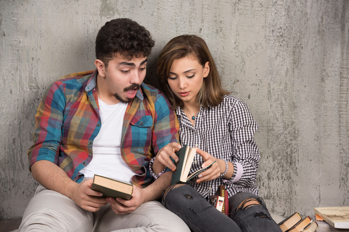 男性坐在地板上拿着书微笑着的年轻夫妇在一起青春女人
