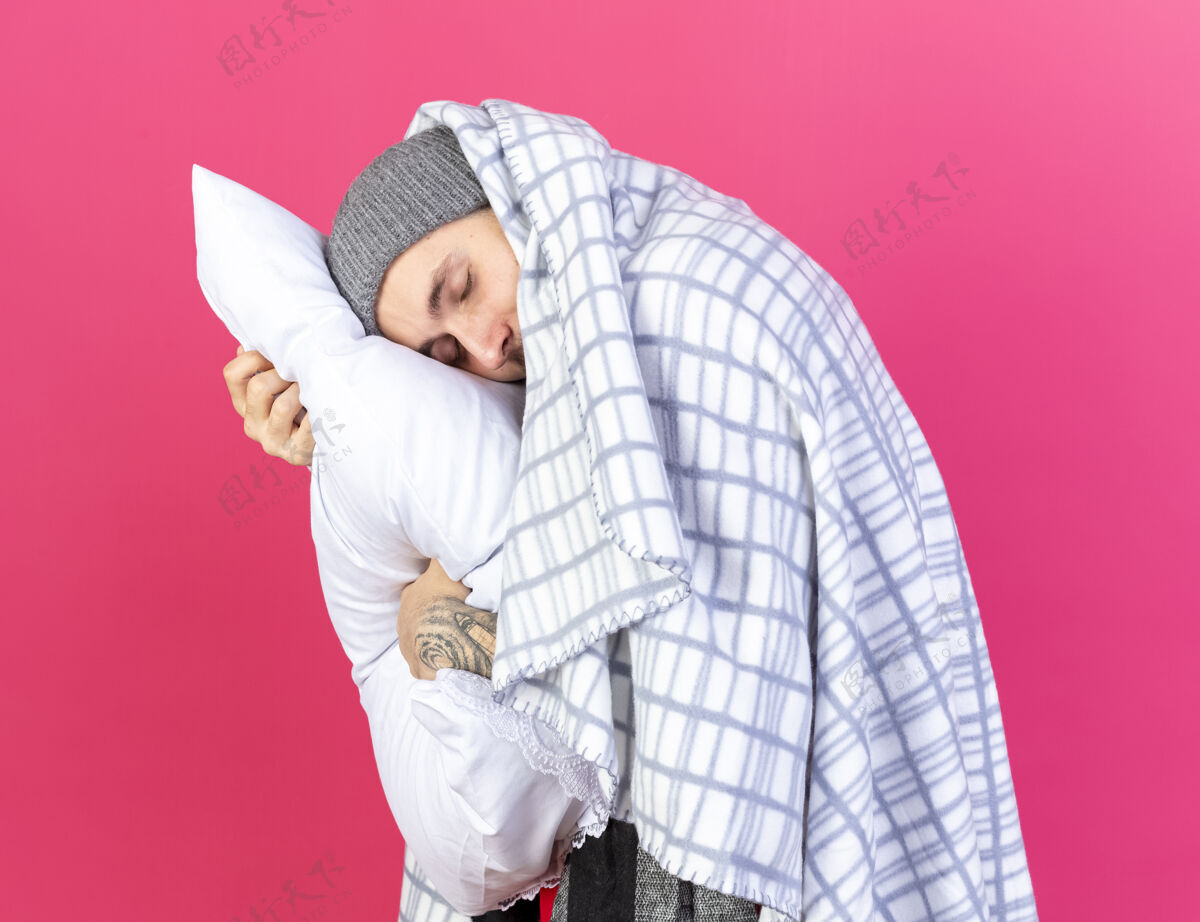 年轻人昏昏欲睡的年轻白种人 戴着冬天用格子布包起来的帽子 把头放在枕头上 隔离在粉红色的墙上 留着复印空间帽子枕头疾病