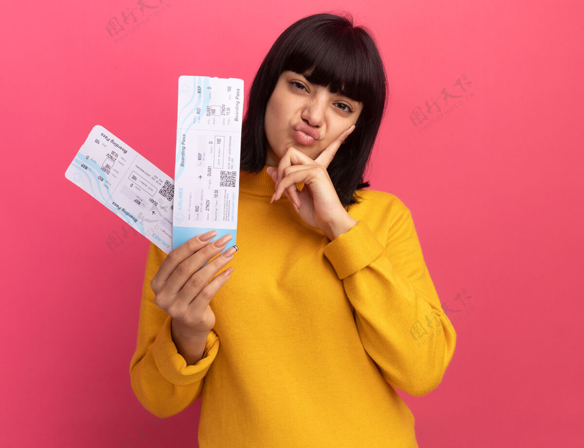 飞机一个年轻的黑发白人女孩把手放在下巴上 手里拿着粉红色的机票手黑发机票