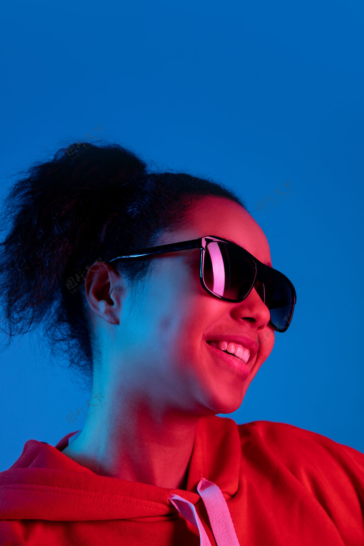明亮耳机在五彩霓虹灯下的蓝色工作室背景上孤立的非洲裔美国女性肖像美丽的女性模特人类情感的概念 面部表情 销售 广告 时尚热带移动成功
