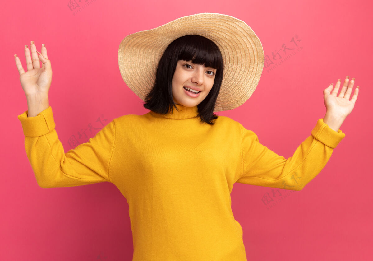深褐色令人印象深刻的年轻黑发白人女孩戴着沙滩帽站在粉红色的举手印象年轻帽子