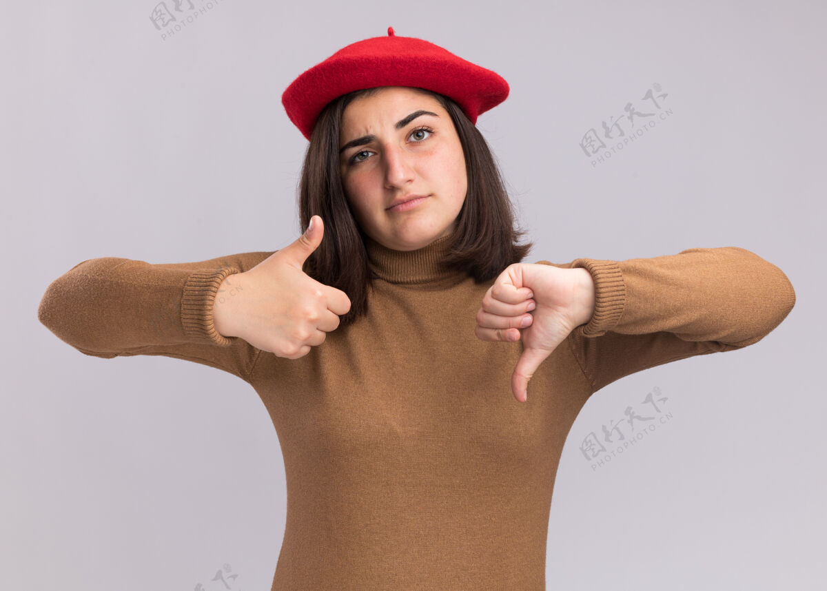 帽子自信的年轻漂亮白人女孩戴着贝雷帽 大拇指朝上 大拇指朝下对着白色女孩自信白色