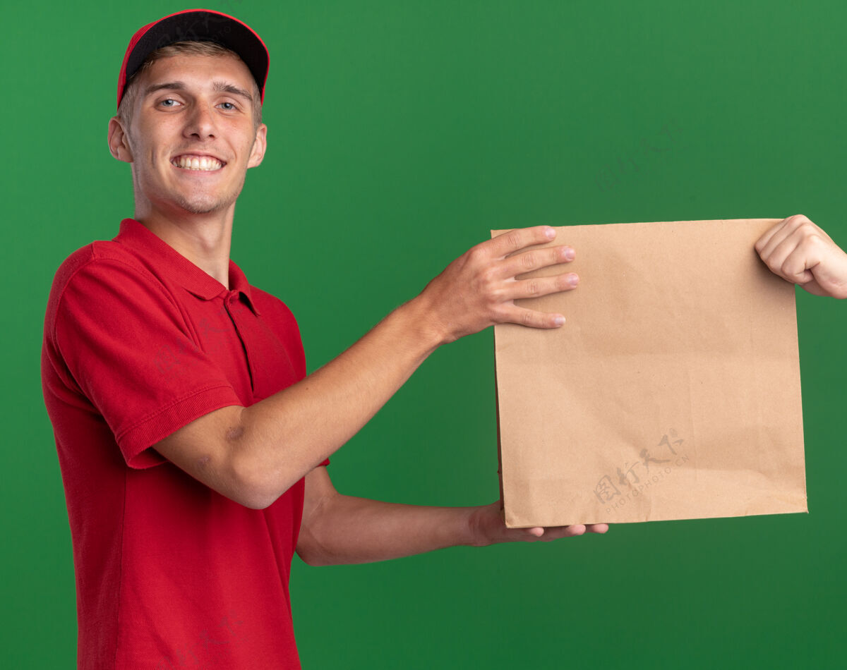 送货微笑着的年轻金发送货员把纸包递给别人 看着绿色的相机给予金发微笑